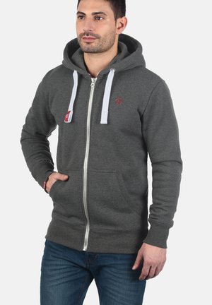 Grijze hoodie met rits, voorzien van een voorzak, witte trekkoorden en een klein rood logo op de borst. Ribgebreide manchetten en tailleband.