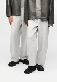 Γκρι φόρμα με άνετη εφαρμογή και ελαστική μέση, σε συνδυασμό με μαύρα παπούτσια με χοντρή σόλα. Το φόντο είναι απλό λευκό.