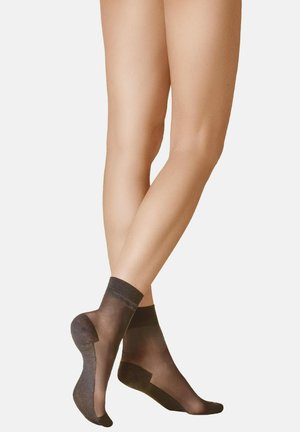 Legs crossed at calves wearing sheer black ankle socks with reinforced toes and heels against a plain background.