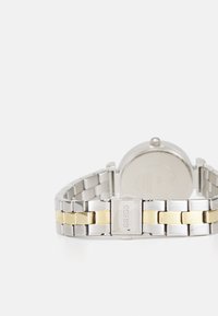 Bracciale in acciaio inossidabile argento e oro con un design a doppio tonfo, dotato di un quadrante rotondo e dettaglio della chiusura.