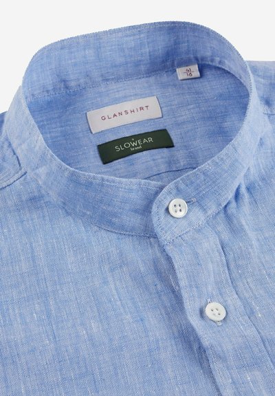 Hellblaues Leinenhemd mit Stehkragen, ausgestattet mit zwei weißen Knöpfen und Etiketten für "GLANSHIRT" und "SLOWEAR" im Kragen.