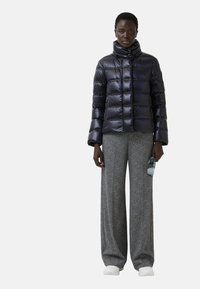 Kurtka puchowa w błyszczącym granacie z wysokim kołnierzem i poziomym pikowaniem, w połączeniu z szerokimi spodniami w szary wzór i białymi butami.