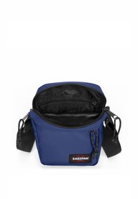 Modrá taška Eastpak vyrobená z odolné tkaniny, s zipovým vrchem, nastavitelným popruhem a černým interiérem. Název loga na přední straně.