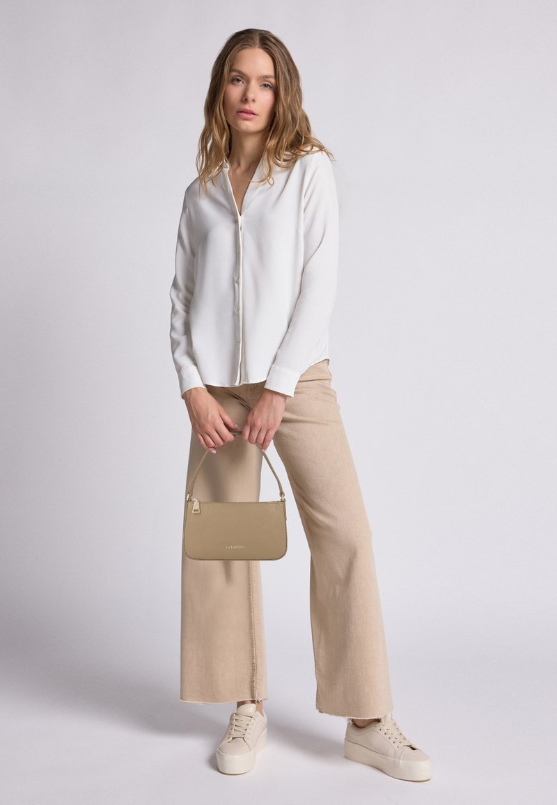 Camicia bianca a bottoni, pantaloni beige a gamba larga, sneakers chiare e una piccola borsa beige. Tessuto liscio con dettagli minimi.