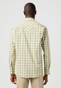 Camicia a maniche lunghe a quadri verde chiaro con yoke in stile western, polsini a bottoni e orlo curvo. Il tessuto appare leggero e testurizzato.