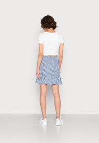 Top cropped branco de manga curta combinado com uma saia rodada azul e branca com listras e bainha com babados. Completado com sapatos brancos.