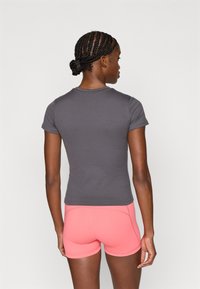 Maglietta grigia aderente a maniche corte abbinata a pantaloncini sportivi rosa acceso. Tessuto liscio, design semplice e colori a contrasto.