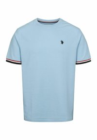 Svetlomodré tričko s krátkym rukávom s čiernym, červeným a bielym prúžkovaným lemovaním na rukávoch a malým čiernym vyšitým logom na ľavej hrudi.