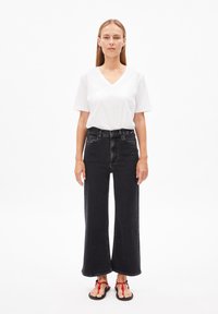 Zwarte wijde spijkerbroek met een hoge taille, gecombineerd met een witte V-hals t-shirt. Zwarte sandalen met rode gevlochten accenten.