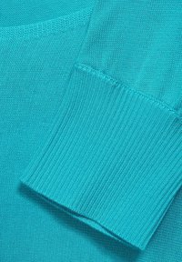 Tyrkysová pletená látka zblízka s detaily ribbed manžety. Hladký povrch s konzistentním vzorem, který ukazuje živou barvu.