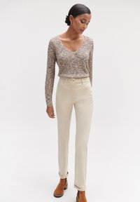 Beige hoge taille fitted broek, gecombineerd met een lichtbruine gebreide trui en bruine enkelboots. Eenvoudig, hedendaags ontwerp.