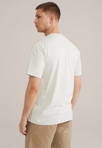 Fehér pamut póló rövid ujjakkal, kerek nyakkal és sima textúrával. A modellen khaki rövidnadrág van, ami laza illeszkedést mutat.