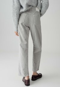 Pantaloni in velluto a coste grigi chiaro con una vestibilità rilassata, caratterizzati da tasche applicate e gamba ampia. Abbinati a mocassini scuri e a un maglione grigio morbido.