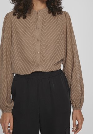 Brązowa bluzka na guziki z wzorem w jodełkę, długie rękawy, elastyczne mankiety, w zestawie z czarnymi spodniami z elastycznym pasem.