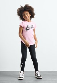 Rosa t-skjorte med korte ermer fra Nike med svart logo, kombinert med svarte leggings med hvit swoosh. Brukt med høye sneakers.