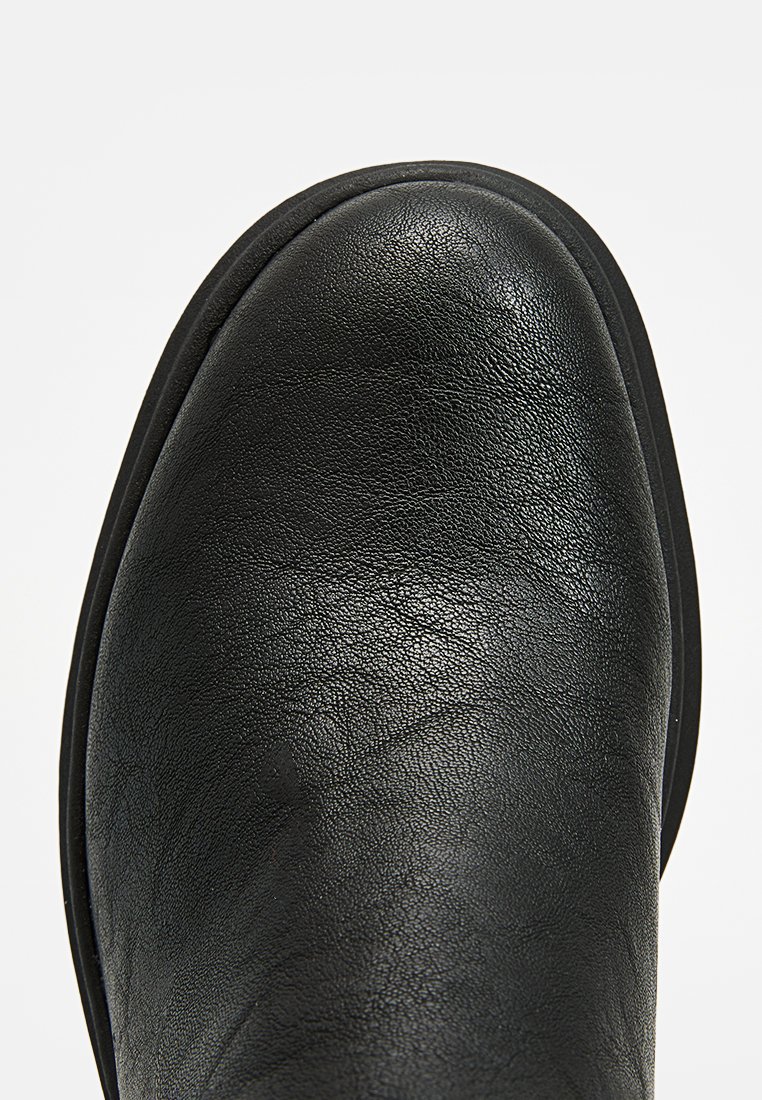 Bottines en cuir noir avec un bout arrondi, présentant une surface légèrement texturée et une semelle en caoutchouc noir solide.