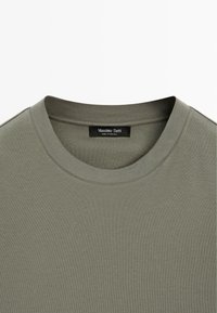 T-shirt à col rond vert olive avec un col surpiqué et une étiquette noire visible portant l'inscription "Massimo Dutti Made in Portugal".
