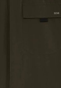 Camicia verde oliva con una texture liscia, caratterizzata da una tasca applicata sul lato sinistro e un piccolo logo in alto a destra.