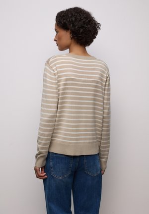 Pull beige à rayures avec des lignes horizontales crème, col et poignets côtelés, coupe courte, associé à un jean bleu à coupe ample.