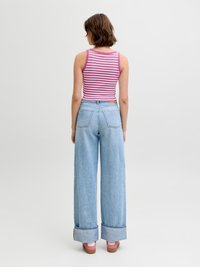 Γυναίκα που φαίνεται από πίσω, φορώντας μια ροζ και λευκή ριγέ φανέλα χωρίς μανίκια, ανοιχτό μπλε παντελόνι με φαρδιά μπατζάκια και ροζ αθλητικά παπούτσια.