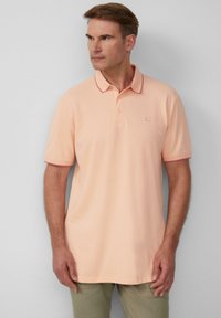 Poloshirt in hellem Pfirsichton mit kontrastierenden roten Akzenten am Kragen und an den Ärmeln, kurze Ärmel, flach gestrickter Kragen, Logo auf der oberen linken Seite.