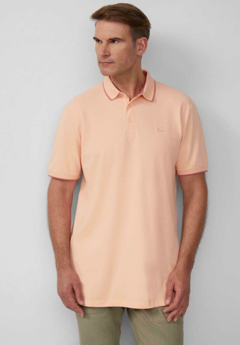 Poloshirt in hellem Pfirsichton mit kontrastierenden roten Akzenten am Kragen und an den Ärmeln, kurze Ärmel, flach gestrickter Kragen, Logo auf der oberen linken Seite.