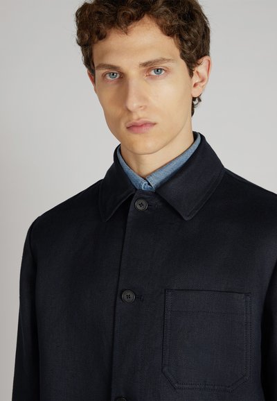 Veste bleu marine avec col, coupe droite et tissu texturé. Présente deux boutons et une poche poitrine sans motifs ni quincaillerie visibles.