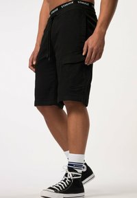 Shorts cargo noirs avec une taille à cordon de serrage, dotés de poches latérales et d'un ourlet replié, associés à des baskets montantes noires et des chaussettes blanches.