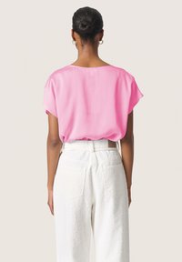 Blusa rosa de manga corta con cuello en la parte posterior, hecha de tejido ligero, combinada con pantalones blancos de tiro alto, holgados y texturizados, que cuentan con bolsillos traseros.