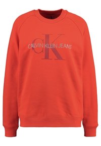 Sudadera roja con cuello redondo, mangas largas de raglán y puños de canalé. Presenta el logo 'CALVIN KLEIN JEANS' en un tono más claro en el pecho.