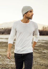 Hvid langærmet skjorte med rund halsudskæring, parret med mørke jeans og en lysegrå strikbeanie. Udendørs omgivelser med sløret baggrund.