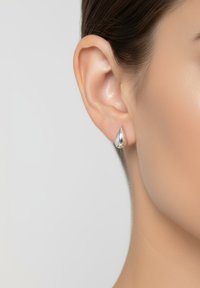 Orecchini a forma di goccia in argento, in metallo lucido con una superficie liscia, entrano in contatto con il lobo dell'orecchio, esaltando il contorno dell'orecchio.