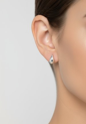 Boucles d'oreilles en argent en forme de goutte, en métal poli avec une texture lisse, touchent le lobule de l'oreille, mettant en valeur le contour de l'oreille.