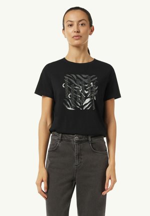 Schwarzes Baumwoll-T-Shirt mit metallic bedrucktem Design, das Streifen und Punkte zeigt, kombiniert mit dunkelgrauen Jeans.