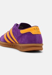 Purple suede sneaker with yellow leather accents, featuring three yellow stripes, rubber sole, and Adidas logo on the heel.