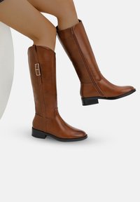 Bruna knähöga stövlar med en slät imitation läder finish, sidogdragkedja och en låg blockklack, med en dekorativ spänne på sidan.