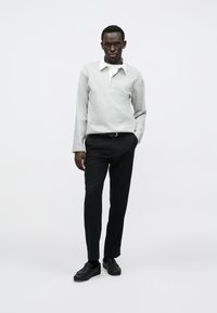 Helehallikas pikkade varrukatega polo-särk valge kraega, kolme nupuga, kombineeritud mustade kohandatud pükste ja mustade loafers-kingadega.