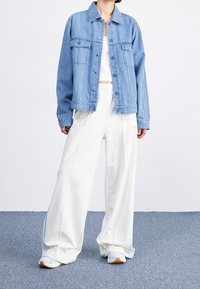 Light blue denim jacket with chest pockets, white tank top, cream wide-leg pants, gray sneakers with orange accents. Flat textile background.