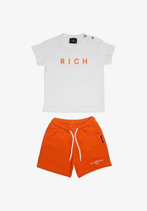 Maglietta bianca a maniche corte per bambina con scritta arancione "RICH" e pantaloncini con elastico in vita arancione, coulisse bianca e piccolo logo bianco.