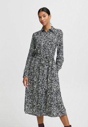 Robe chemise à motifs noir et blanc avec des manches longues, un col, une ceinture à la taille et des poches latérales, en tissu léger.