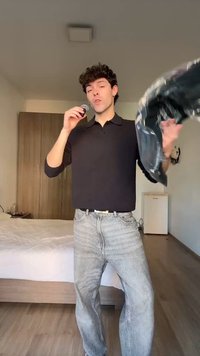 Noor mees mustas särgis ja teksades sööb küpsist ning hoiab musta plastkotti magamistoas, kus on puidust riidekapp ja voodi.