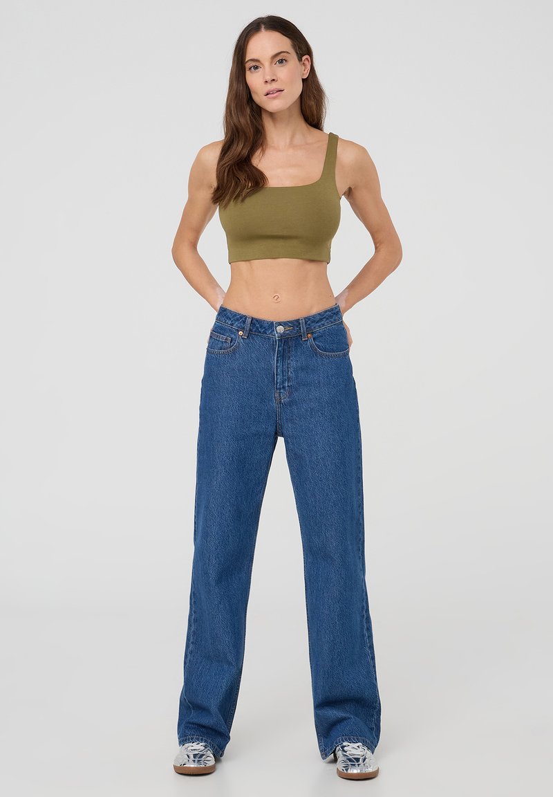 Top corto color verde oliva abbinato a jeans blu a vita alta e gamba larga. Denimb strutturato, con un classico design a cinque tasche.