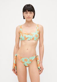 Ensemble de bikini à motif tropical mettant en avant un fond vert menthe avec des motifs floraux orange. Le haut est doté de larges bretelles ; le bas est de style à nouer sur les côtés.