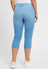 Lichtblauwe denim capri jeans met een middelhoge taille, twee achterzakken en een schone zoom, gecombineerd met witte sneakers.