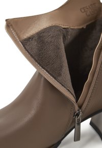 Botín de cuero marrón con un interior suave, cremallera lateral y detalles de costura sutiles en la costura superior. Tacón no desmontable.