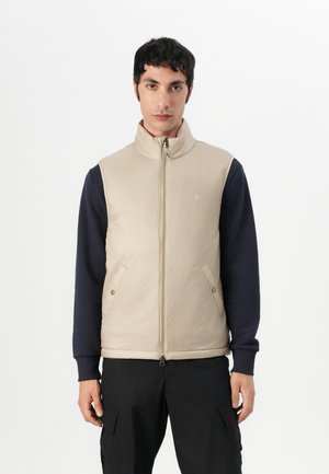 Gilet isolant beige avec un col montant et une fermeture éclair, doté de poches à pression, associé à une chemise navy à manches longues. Design plat, texture lisse.