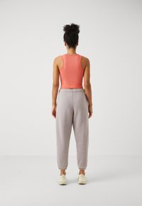 Koral ermeløs topp kombinert med lyse grå joggebukser. Joggebuksene har strikk i livet og avsluttende ankler for en behagelig passform.