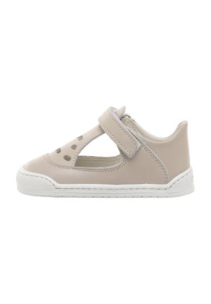 Zapato de piel beige con recortes, correa de Velcro y suela de goma blanca. Presenta punta redonda y acentos de costura a lo largo de los bordes.
