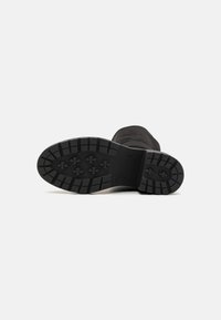 Semelle en caoutchouc noir avec un motif de tread texturé, présentant des rainures et des crêtes profondes pour une meilleure adhérence. Forme plate et arrondie sans aucune marque visible.