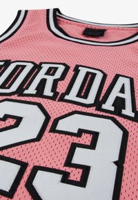 Ροζ μπασκετική φανέλα με υφή από δίχτυ, μαύρες λεπτομέρειες και κεν τημένα τα γράμματα "JORDAN" και ο αριθμός "23" σε λευκό με μαύρο περίγραμμα.